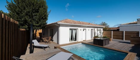 Une piscine dotée d’une terrasse en bois, de chaises longues et d’un petit bâtiment surmonté d’un toit en tuiles.