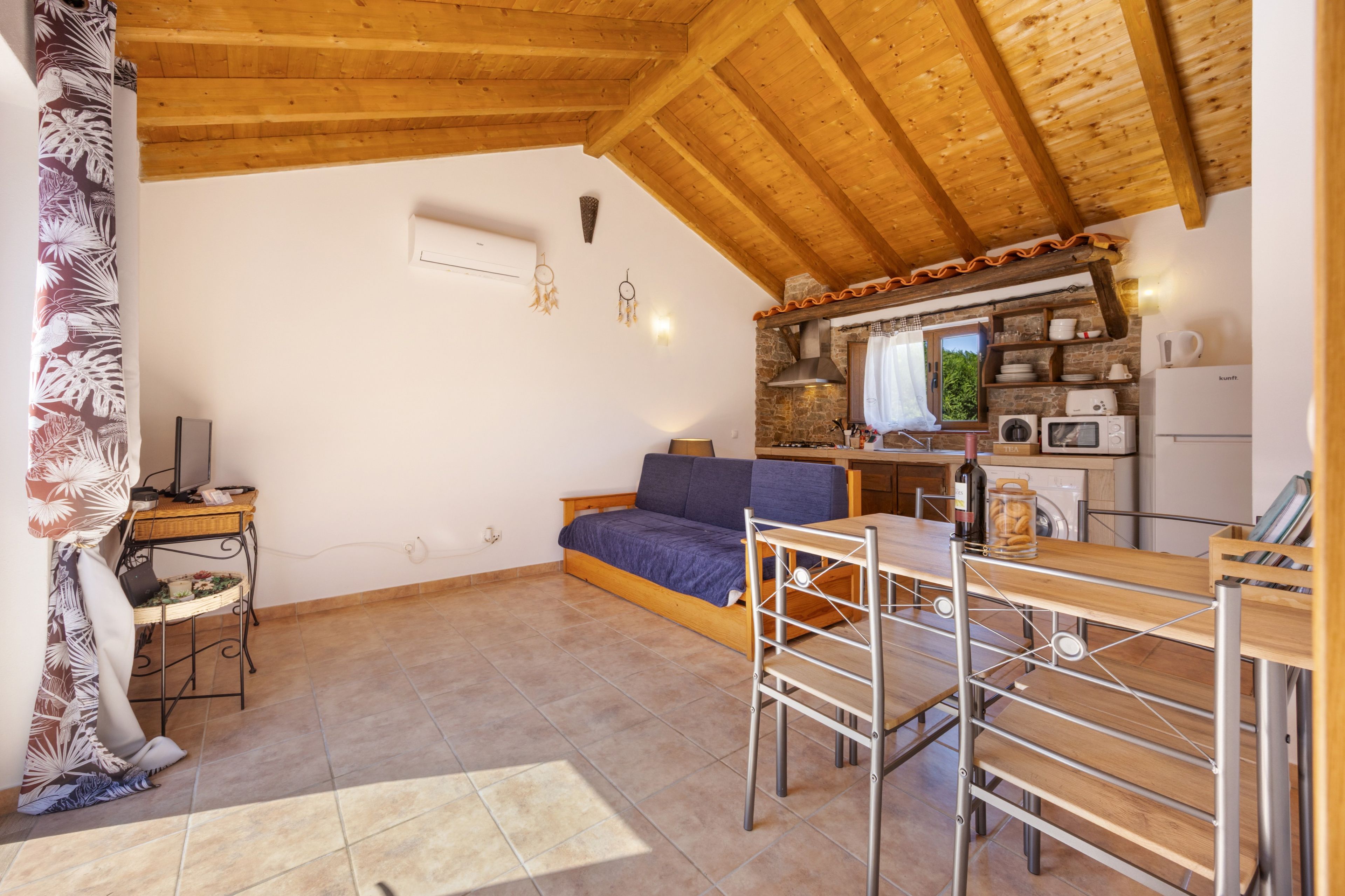 A compact living space with a wooden ceiling, a sofa, a dining table, and a kitchenette.
