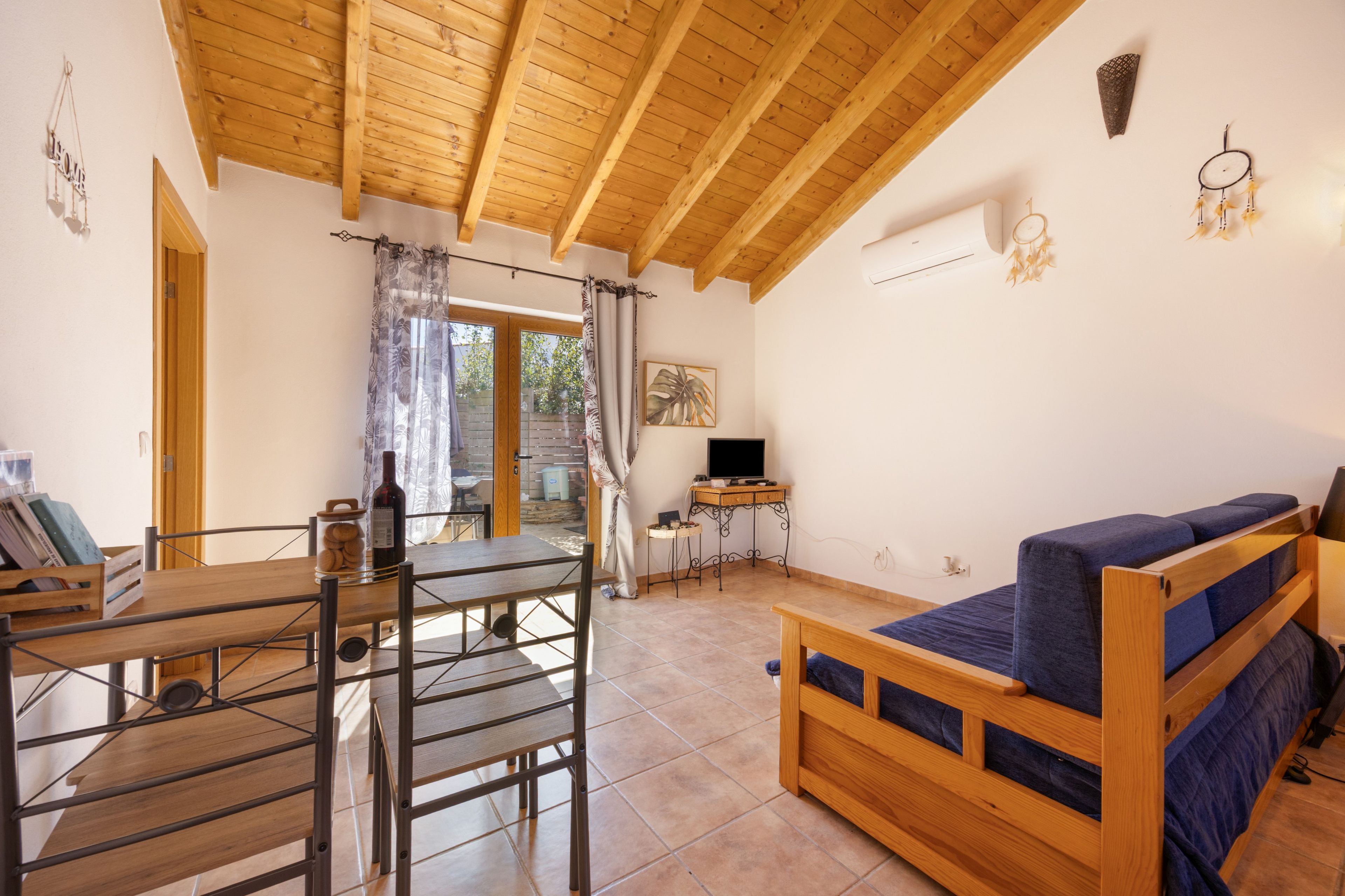 Une pièce avec un plafond en bois, un lit avec une literie bleue, une table avec une bouteille et un téléviseur posé sur un meuble.