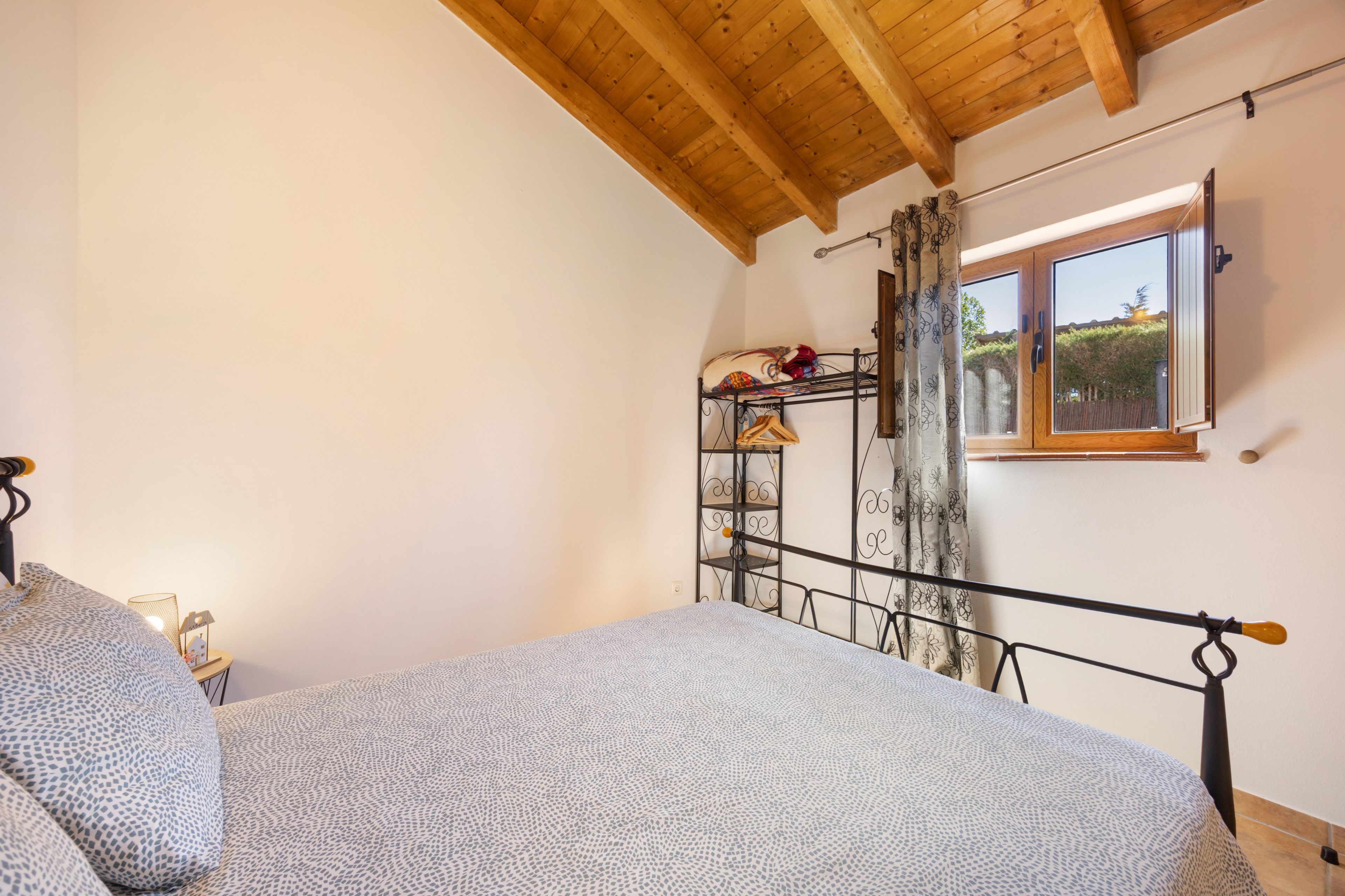 A bedroom with a bunk bed, a window with a view of greenery, and a metal shelf unit with hanging items.