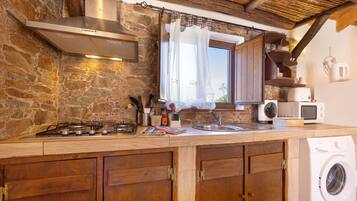 A rustic kitchen with a stone wall, wooden cabinets, a gas stove, a sink, and a washing machine.