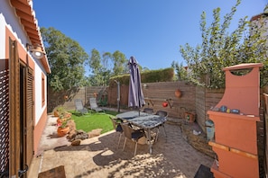 A patio with a table and chairs, a barbecue grill, and a wooden fence.