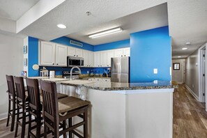 A kitchen with white cabinets, a stainless steel refrigerator, and a blue accent wall. - Paradise 510 - Oceanfront 3BR Condo w/ Pool (Myrtle Beach)