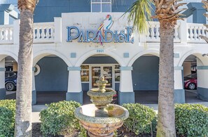 A building with a sign reading "PARADISE" and the number "2201" above the entrance. There is a decorative fountain in front of the building. - Paradise 510 - Oceanfront 3BR Condo w/ Pool (Myrtle Beach)