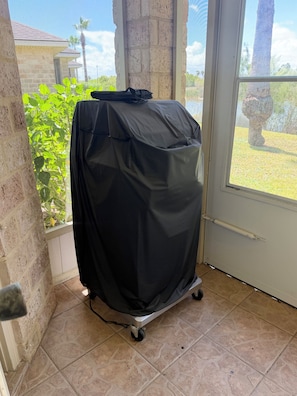A covered grill on wheels in a corner with a view of a house and palm trees outside. - The Lake Breeze Villa- 48GH (Laguna Vista)