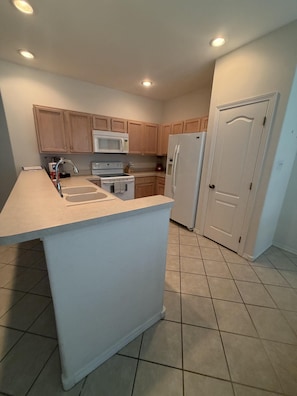 A kitchen with wooden cabinets, a white countertop, a microwave, a stove, and a refrigerator. - The Lake Breeze Villa- 48GH (Laguna Vista)