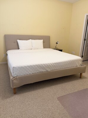 A bed with a headboard, a bedside table with a lamp, and a carpeted floor. - The Lake Breeze Villa- 48GH (Laguna Vista)