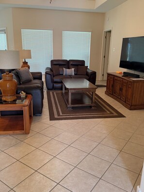 A living room with a sofa, coffee table, TV stand, and a rug. - The Lake Breeze Villa- 48GH (Laguna Vista)