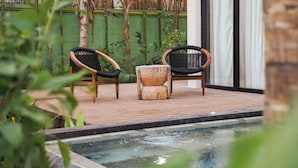 A poolside area with two wicker chairs and a wooden stool.