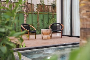 A poolside area with two wicker chairs and a wooden stool.