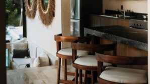 A modern kitchen with a bar area, wooden stools, and a refrigerator.