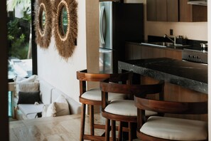 A modern kitchen with a bar area, wooden stools, and a refrigerator.