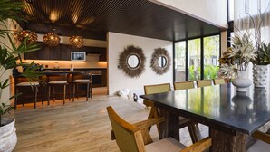 Een moderne eethoek met een grote tafel, houten stoelen en een keuken op de achtergrond.