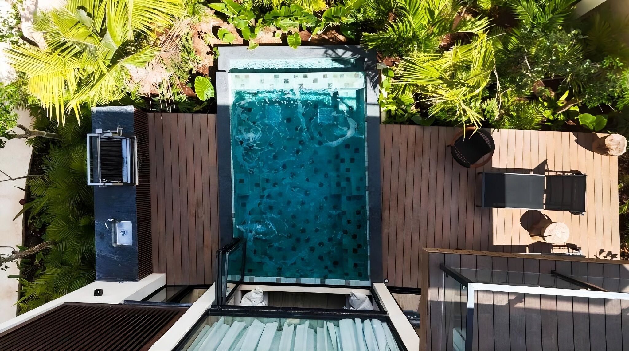 Ein Pool auf dem Dach mit Glasveranda, umgeben von einer Holzterrasse und üppiger Vegetation.