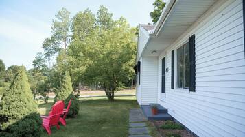 A white house with a covered porch, a small garden with a lawn, and a red chair.