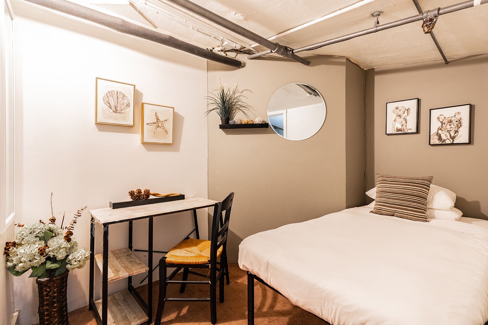 A bedroom with a bed, a desk with a chair, a mirror, and framed pictures on the wall.