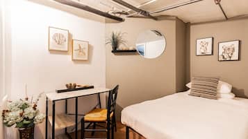 A bedroom with a bed, a desk with a chair, a mirror, and framed pictures on the wall.