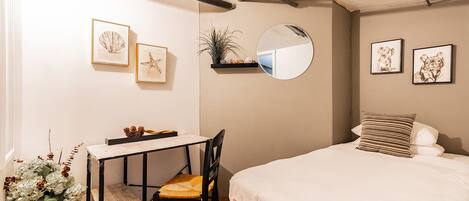 A bedroom with a bed, a desk with a chair, a mirror, and framed pictures on the wall.