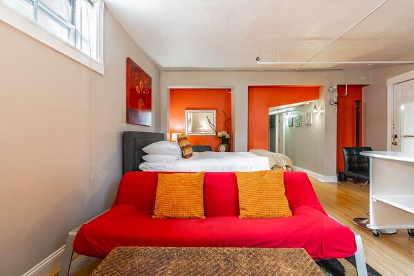 A hotel room with a bed, a red sofa, a desk, and a bathroom visible through an open door.