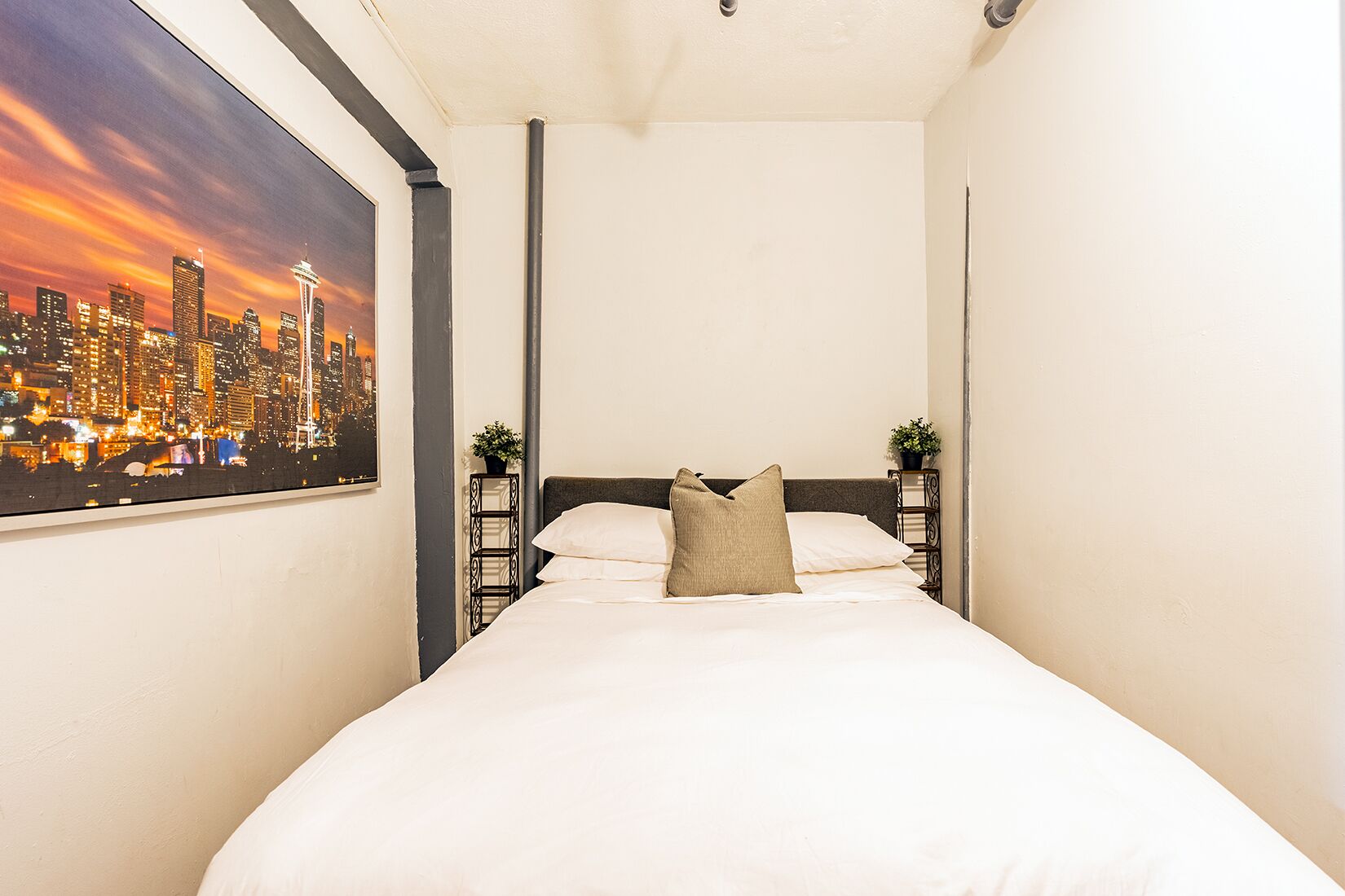 Een hotelkamer met een bed, een stadslandschap schilderij en uitzicht op een nachtelijke hemel.