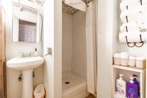 Ein Badezimmer mit einem weißen Waschbecken, einer Dusche und einem Ablagefach mit Toilettenartikeln.