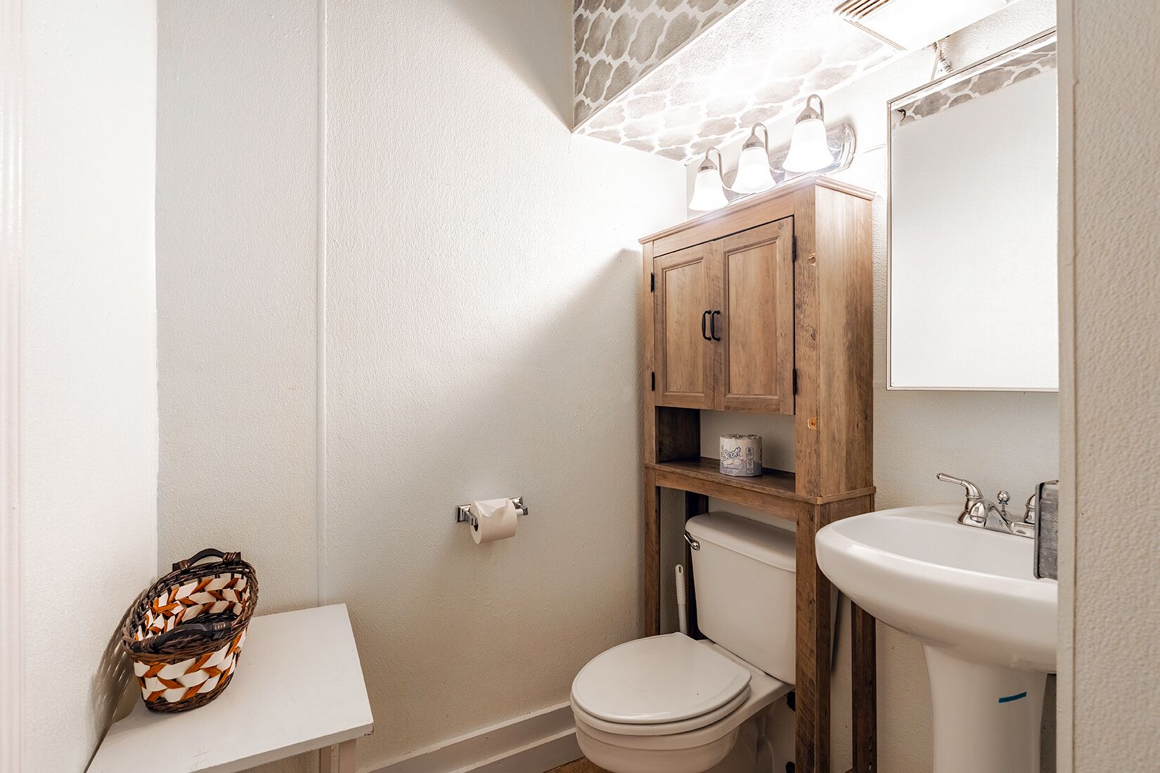 A bathroom with a toilet, a sink, and a wooden cabinet with shelves.