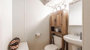 A bathroom with a toilet, a sink, and a wooden cabinet with shelves.