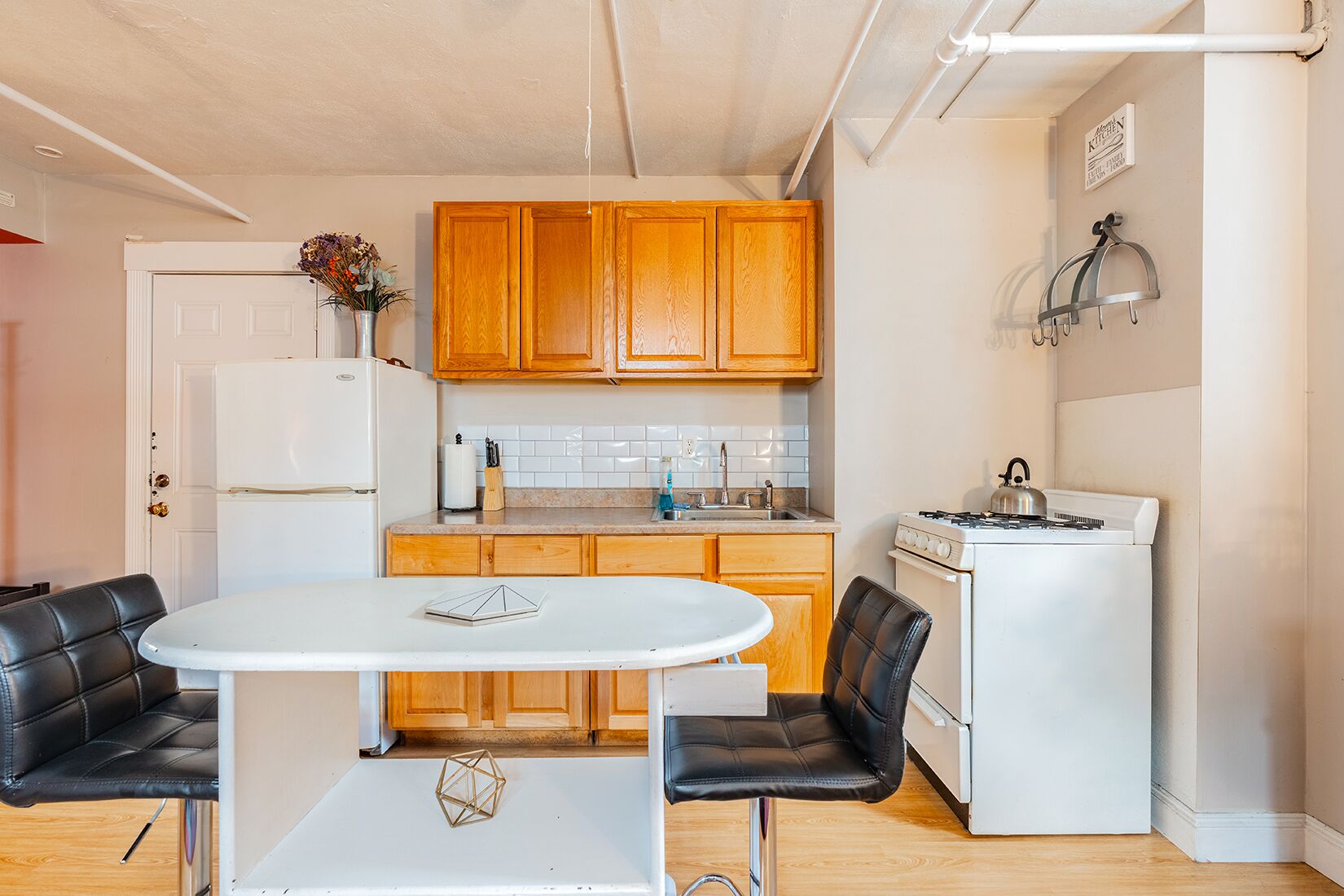 A compact kitchen with wooden cabinets, a white stove, and a dining table with two chairs.