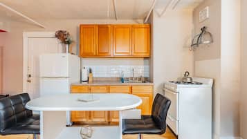 A compact kitchen with wooden cabinets, a white stove, and a dining table with two chairs.