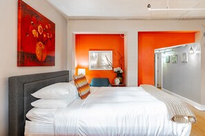 Ein modernes Hotelzimmer mit einem großen Bett, einer grauen Kopfteil und orangefarbenen Akzentwänden.