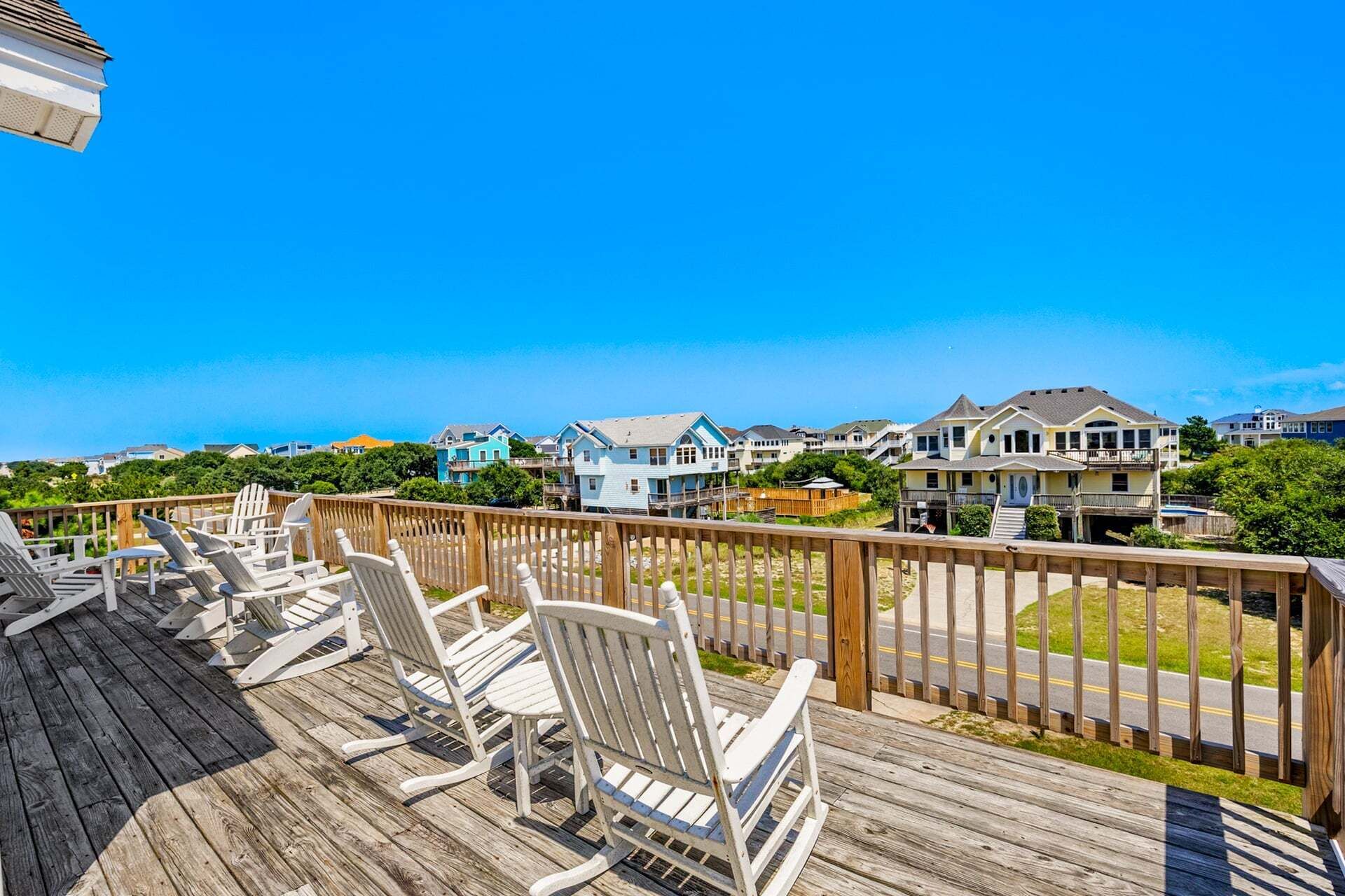 A wooden deck with white chairs and a view of houses and a road.
