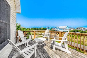A wooden deck with white Adirondack chairs and a small table, overlooking a residential area with houses and a clear sky. - Family Affair Corolla retreat with private pool, hot tub, and easy beach access. (Corolla)