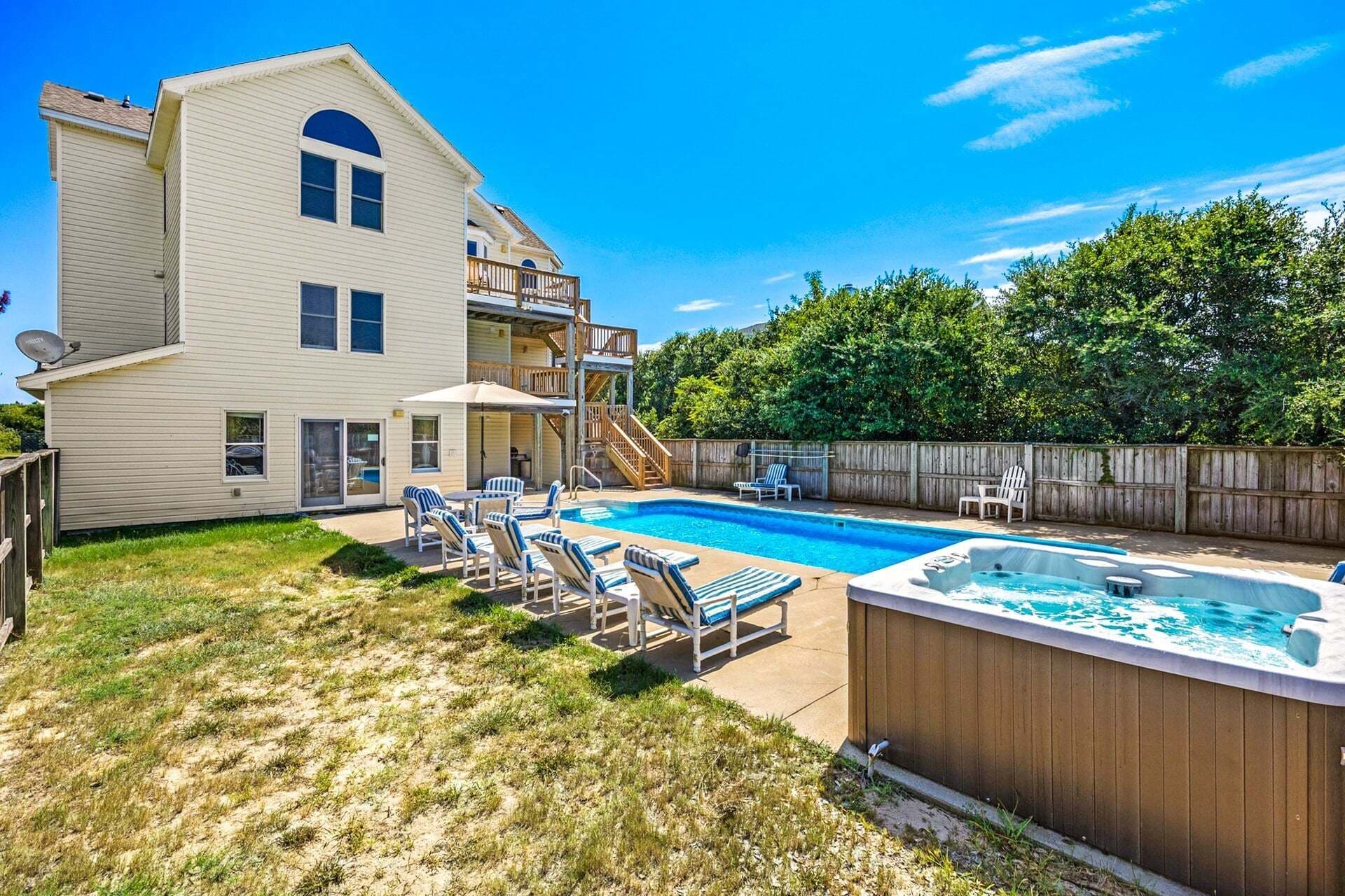 A two-story house with a backyard swimming pool, a hot tub, and a wooden deck with lounge chairs.