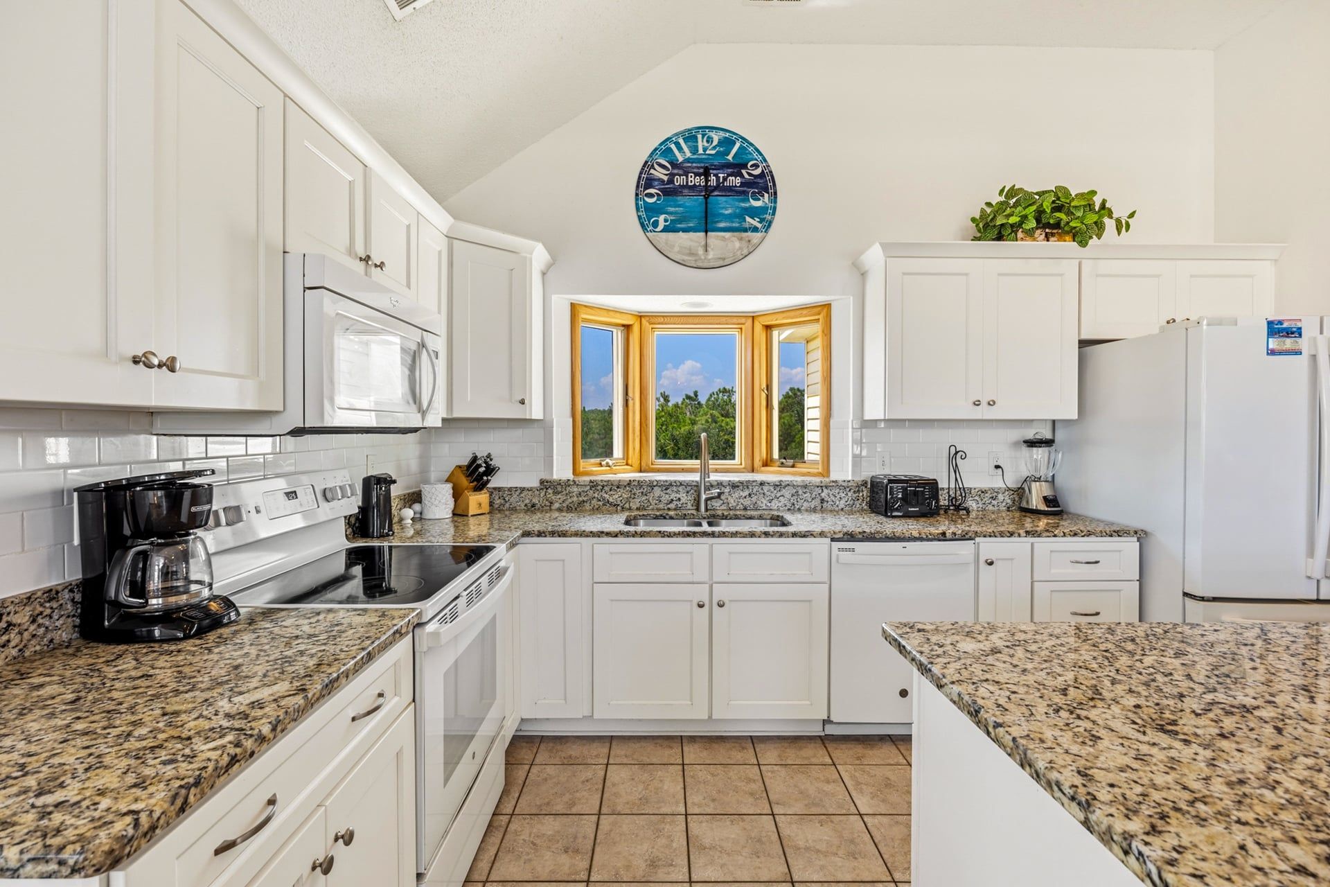 A kitchen with white cabinets, a granite countertop, a coffee maker, a toaster, and a blender.