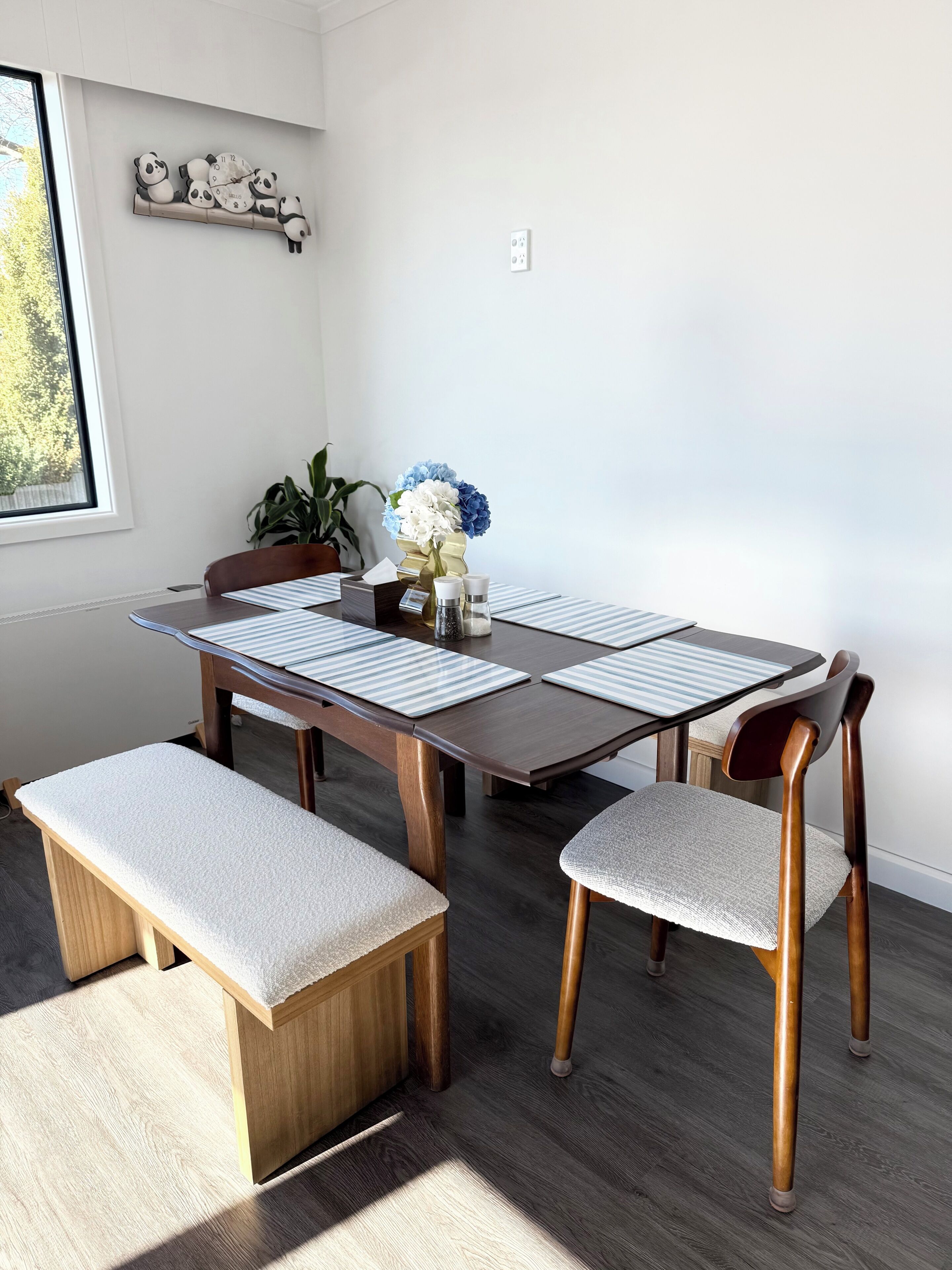 A dining area with a wooden table, cushioned benches, and a decorative wall clock.