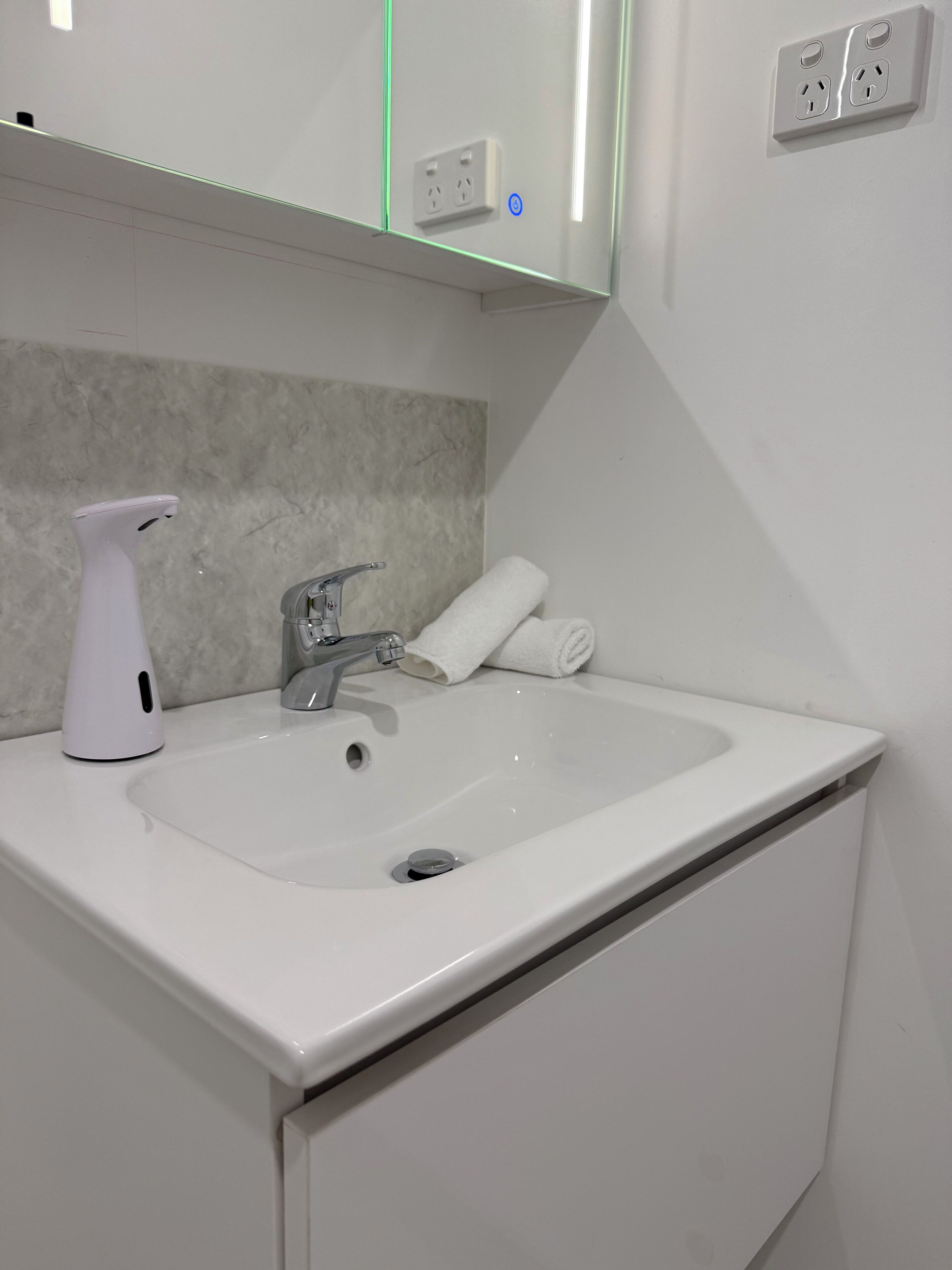Een badkamer met een witte wastafel, een handdouche, een handdoek en een spiegel boven de wastafel.