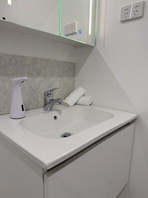 A bathroom with a white sink, a handheld spray bottle, a towel, and a mirror above the sink.