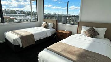 Hotellihuone, jossa on kaksi sänkyä, yöpöytä ja suuret ikkunat, joista avautuu näkymä kaupungin ylle.