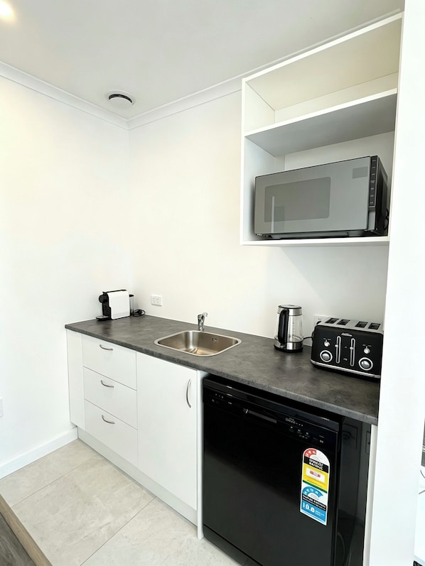 A compact kitchen with a dishwasher, a microwave, and a toaster on the countertop.