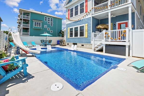 Une piscine avec un toboggan, des chaises longues et un espace de détente.
