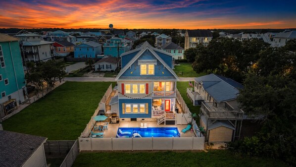 Une maison à deux étages avec une piscine, entourée d’une pelouse bien entretenue et de maisons voisines.