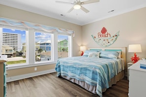 A bedroom with a bed, two bedside lamps, a ceiling fan, and a view of the outside. - NEW 4BR/4BA Beach Retreat, Heated Pool, Slide, Elevator, Bikes, 2 Min to Ocean (Carolina Beach)