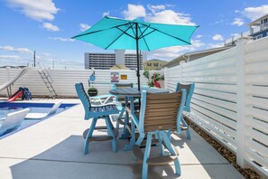 Une terrasse extérieure avec une piscine, une table entourée de chaises et un grand parasol.