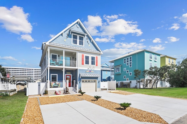 A two-story house with a balcony, a garage, and a well-maintained lawn. - NEW 4BR/4BA Beach Retreat, Heated Pool, Slide, Elevator, Bikes, 2 Min to Ocean (Carolina Beach)