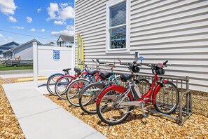 Une rangée de vélos est garée devant un bâtiment à la façade blanche, dont une fenêtre est équipée de stores.