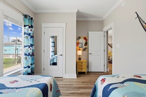 Une chambre avec deux lits, une fenêtre avec des rideaux, une porte, une table de chevet avec une lampe et un élément décoratif mural.