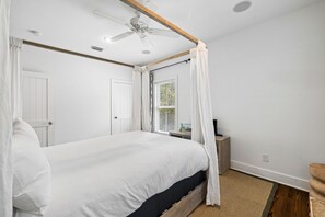 Ein Schlafzimmer mit einem Bett, einem Deckenventilator, einem Fenster mit Jalousien und einem Nachttisch.