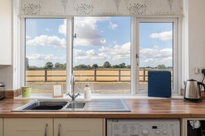 Una cocina con un ventanal amplio, un lavabo y una tetera sobre la encimera.