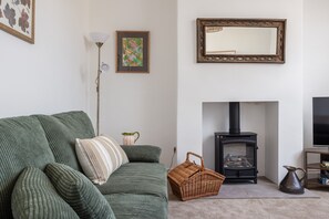 Una sala de estar con un sofá verde, una chimenea, un televisor y un cuadro en la pared.