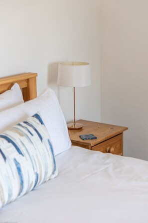 A neatly made bed with white and blue patterned pillows, a wooden bedside table with a white lamp, and a small drawer. - Leys Cottage - sleeps 2 guests (TOPCLIFFE)